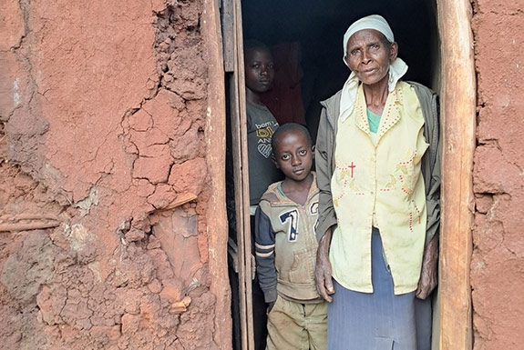 A grandmother standing with her grandchild in her deteriorating home.